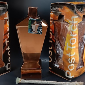 May include: A copper-colored post torch with a square top and base, and a tag that reads "Post Torch." The torch is displayed with its packaging, which features the text "BirdBrain" and a flame design. A white wick is in the foreground.