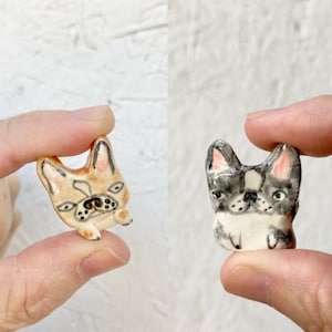 May include: Two ceramic figurines of French Bulldogs. One is beige with black markings and the other is gray with white markings.