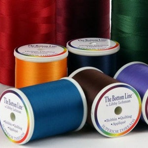 May include: Assortment of spools of The Bottom Line Superior Threads in various colors, including red, orange, blue, brown, purple, and green. The spools are labeled with the brand name and "Superior Threads".