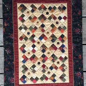 May include: A quilted wall hanging with a diamond pattern in shades of red, blue, green, and brown. The quilt is decorated with buttons and has a dark blue and red border.