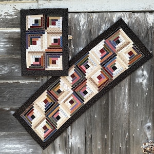 May include: Two quilted table runners in a log cabin pattern. The smaller runner is 12 inches by 16 inches and the larger runner is 12 inches by 48 inches. Both runners have a black background with a cream, brown, and red log cabin pattern.