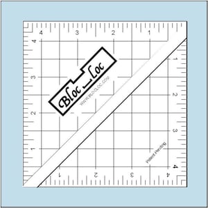 May include: A white and black Bloc Loc quilting ruler with grid lines and diagonal markings. The ruler has measurements in inches and the text "Bloc Loc" and "www.BLOCLOC.COM". The text "Patent Pending" is also visible.