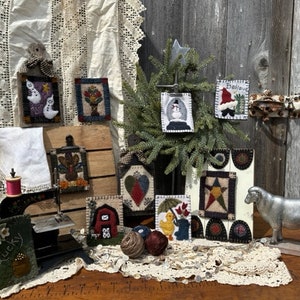 May include: A collection of handmade wool felt ornaments, including a snowman, a turkey, a barn, a heart, a duck, a ghost, a bouquet of flowers, a star, and a sheep. The ornaments are displayed on a wooden table with a vintage sewing machine and a white lace tablecloth.