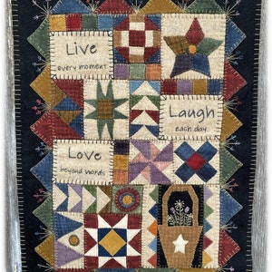May include: A colorful patchwork quilt with a black background. The quilt is made up of squares and triangles in various colors, including red, blue, green, yellow, and brown. The quilt features the words "Live every moment", "Love beyond words", and "Laugh each day".