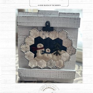 May include: A white felt hexie block with a snowman design. The block is displayed on a white wooden background. The text "Hexigrams" and "A Hexie Block of the Month" is displayed above the block. The text "Hand Made Craft" and "Pastthyme Patterns" is displayed below the block.