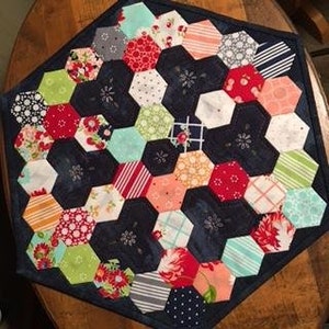 May include: A hexagonal patchwork table runner with a navy blue background and colorful fabric squares in various patterns, including floral, geometric, and polka dots.