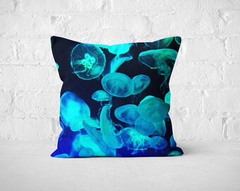May include: Square cushion with a striking design of luminous blue and teal jellyfish on a dark blue backdrop. This decorative cushion is ideal for a bed or sofa, bringing a marine theme to home decor.