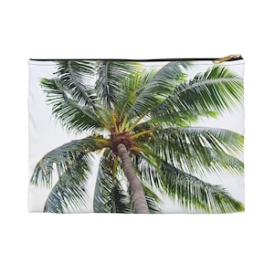 Könnte beinhalten: Eine weiße, rechteckige Tasche mit goldenem Reißverschluss, die ein lebendiges Bild einer Palme zeigt. Der Baum hat grüne Wedel und einen braunen Stamm, vor weißem Hintergrund.