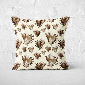 Może przedstawiać: Kwadratowa poduszka dekoracyjna z powtarzającym się wzorem brązowych i kremowych muszli. Poduszka jest umieszczona na białej powierzchni przed białą ceglaną ścianą. Muszle mają skomplikowane detale.