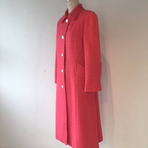 May include: A long, bright pink coat with a button fastening and a collar. The coat is made of a textured fabric and has a simple, classic design.