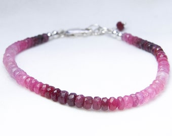May include: A delicate bracelet made with faceted pink and red gemstones, graduating in color from light pink to deep red. The bracelet is strung on a silver chain with a lobster clasp.