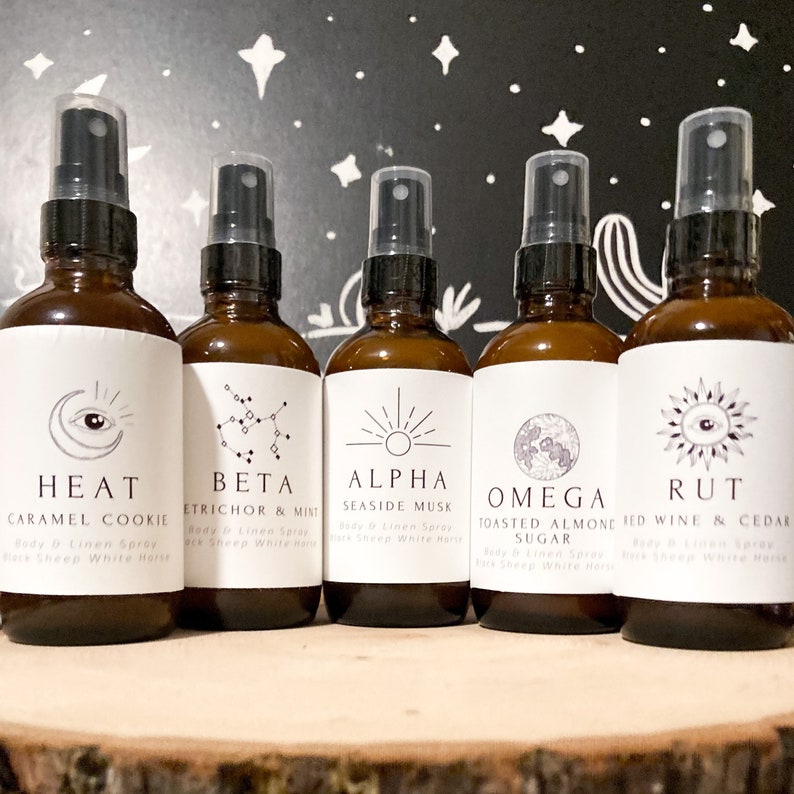 May include: Five amber glass bottles with spray tops and white labels. Each bottle has a different scent and a unique symbol on the label. The scents are Heat Caramel Cookie, Beta Etricor & Mint, Alpha Seaside Musk, Omega Toasted Almond Sugar, and Rut Red Wine & Cedar.
