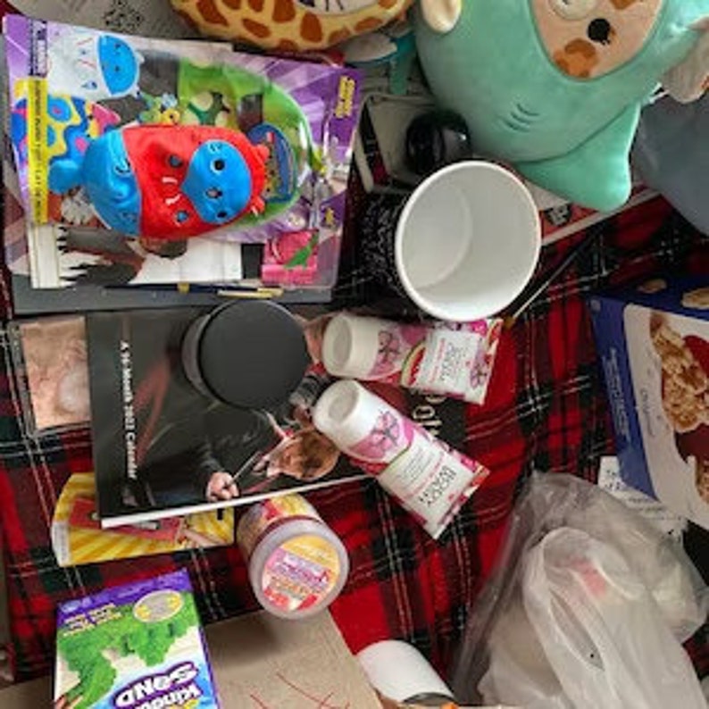 以下が含まれることがあります： 黒と白の本、黒い瓶、ピンクのローションのチューブ2本、白いマグカップ、青と赤のぬいぐるみ、ピンクと緑のぬいぐるみ、シリアル箱、スナッククラッカーの箱、雑誌など、さまざまなアイテムのコレクションです。