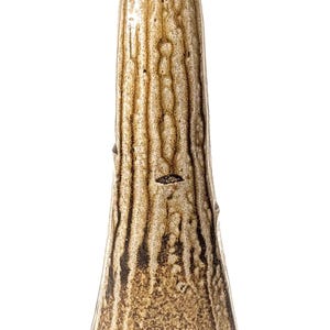 May include: A tall, tapered ceramic vase with a textured, mottled brown and tan glaze. The surface features vertical, drip-like patterns in darker brown tones, creating a rugged, organic appearance with a narrow opening at the top.