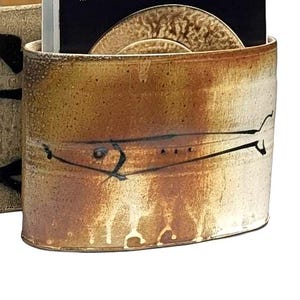May include: Two ceramic magazine holders with a rustic design. One is tan with black stripes, the other is brown with black accents. Each holder contains a magazine with the word "ceramics" on the cover.