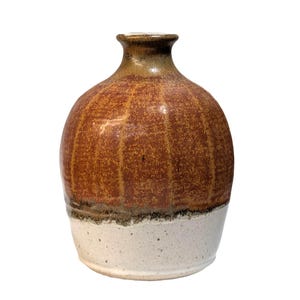 May include: A handcrafted ceramic vase with a rounded body and a narrow neck. The upper portion is a warm brown with vertical textured lines, transitioning to a speckled white base. The vase is approximately 7 inches tall.