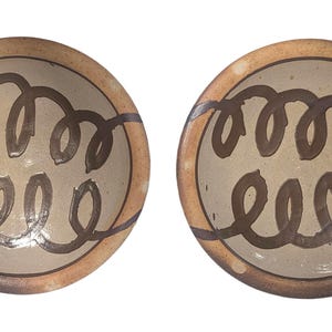 May include: Two round ceramic bowls featuring a light beige interior with a dark brown hand-painted spiral design. The rims are a contrasting toasted brown color with subtle white speckles, creating a distinct border around the central pattern.