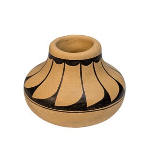 May include: A small, round, beige ceramic vase with a wide opening. The vase is decorated with black, curved, petal-like shapes around the body and a scalloped black band at the top. The vase is isolated on a white background.
