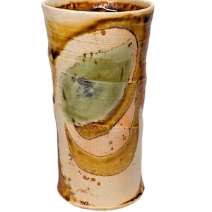 May include: A handmade ceramic tumbler with a unique, organic design. The beige-colored cup features abstract patterns in shades of green, brown, and orange. The tall, cylindrical shape is ideal for beverages. The tumbler is approximately 6 inches tall.