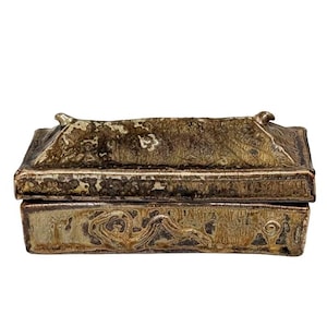 May include: A small, rectangular antique box with a hinged lid. The box is made of a tarnished, aged metal with intricate embossed designs on the sides and top. The box has a weathered appearance, suggesting age and use.