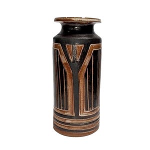 May include: A ceramic vase with a dark brown and tan geometric design. The vase has a cylindrical shape with a flared top and base. The design features vertical lines and a central Y-shaped element.