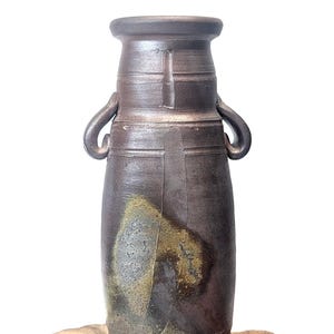 May include: A tall, cylindrical ceramic vase with a dark, metallic brown finish and two small, curved handles on the upper sides. The surface features a textured, mottled patch of muted yellow and gray glaze near the base and mid-section.