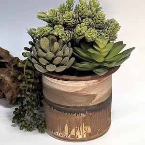May include: A ceramic planter with a textured, earthy design, filled with an assortment of artificial succulents in shades of green and gray. The planter has a brown and beige color scheme, creating a natural aesthetic.