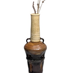 May include: A handcrafted ceramic vase with a tall, slender neck and a bulbous base. The vase features a two-tone color scheme, with a light beige neck and a dark brown base. Dried lavender stems are placed inside the vase.
