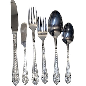 May include: A set of six silver-toned stainless steel flatware pieces including a dinner knife, a butter knife, two forks of varying sizes, a dinner spoon, and a teaspoon. Each handle features an embossed floral and leaf pattern design.