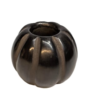May include: A dark, glossy ceramic vase with a rounded, pumpkin-like shape. The vase has vertical ridges and a wide opening at the top. The color is a deep, charcoal gray with subtle highlights.