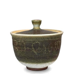 May include: A ceramic bowl with a lid. The bowl is a dark brown color with green and white accents. The lid has a small handle. The bowl has a textured surface and a round shape. The bowl is likely used for serving food.