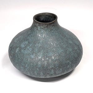 May include: A round, textured vase with a wide body and a narrow opening. The vase has a mottled teal and gray finish with a dark brown rim. The ceramic vessel is suitable for displaying flowers or as a decorative accent.