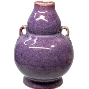 May include: A purple ceramic vase with a double-gourd shape, featuring two small handles. The vase has a speckled texture and a glossy finish, with a slightly lighter rim. The base is a darker shade of purple.