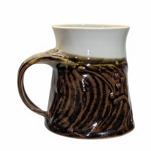May include: A handmade ceramic mug with a brown and white glaze. The mug features a textured, dark brown pattern on the lower half and a smooth, white interior. The handle is a curved, dark brown color.