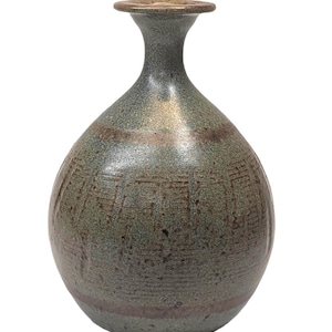 May include: A round ceramic vase with a narrow neck and a flared rim. The surface features a mottled grey-green glaze with subtle brown horizontal bands and vertical etched lines that wrap around the body of the vessel, creating a textured appearance.
