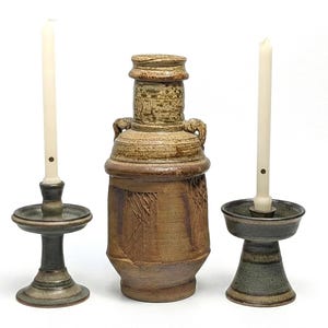 May include: Three ceramic candle holders and a decorative vase. The candle holders are in shades of green and brown, with tall, slender white candles. The vase is a tall, textured brown with a detailed top.