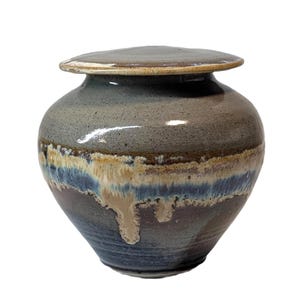 May include: A handcrafted ceramic jar with a lid. The jar has a rounded body and a lid that sits on top. The color scheme includes shades of blue, brown, and beige, with a glossy finish. The jar is likely used for storage or decorative purposes.
