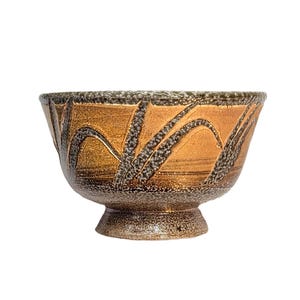 May include: A ceramic bowl with a pedestal base. The bowl features a warm, golden-brown glaze with a textured, dark gray and black leaf-like pattern. The rim has a textured, dark gray border.