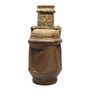 May include: A handcrafted, brown ceramic vase with a textured surface and a unique design. The vase features a cylindrical body with carved patterns, a wide base, and a detailed top section with two small handles. The vase is approximately 12 inches tall.