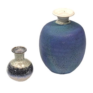 May include: Two ceramic vases with a glossy finish. The larger vase is a deep blue with a textured surface, and a white rim. The smaller vase has a speckled, multi-toned appearance with shades of gray, black, and white.