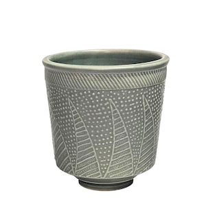 May include: A gray ceramic cup with a textured surface and a decorative leaf pattern. The cup has a rounded rim and a small, circular base. The design features a series of stylized leaves and small dots.