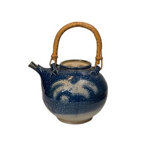 May include: A round ceramic teapot featuring a deep blue glaze with white speckled accents and a gradient effect toward the base. The teapot includes a curved spout and a tall, arched handle made of light brown textured bamboo material.