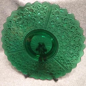 May include: A vintage green glass serving dish with a scalloped edge and a central raised section. The dish is divided into three sections and features a detailed starburst pattern. The glass has a rich, emerald green color.