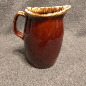May include: A brown ceramic jug with a white glazed rim. The jug has a rounded body and a handle.
