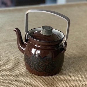 May include: A brown enamel teapot with a silver handle and lid. The teapot has a black floral design.