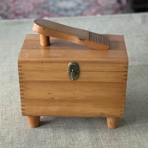 Puede incluir: Una caja de madera para lustrar zapatos con reposapiés incorporado. La caja es rectangular con juntas de cola de milano y un cierre de latón. El reposapiés es una pieza separada de madera con una superficie ranurada.