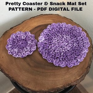 May include: A set of two crocheted purple coasters, one larger than the other, on a wooden surface. The coasters are made with a variegated purple yarn and have a circular shape.
