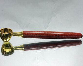 May include: A gold-coloured coffee scoop with a wooden handle. The handle is a deep red colour with a wood grain pattern.