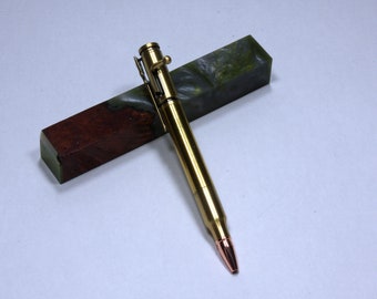 May include: A gold-coloured pen made from a bullet casing with a copper tip. The pen is resting on a block of green and brown resin.