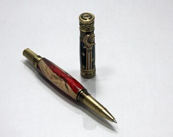 May include: A wooden pen with a brass tip and a red, white and blue design. The pen is closed and the cap is off. The cap is brass with a gold eagle and the words "God Bless America" on it.